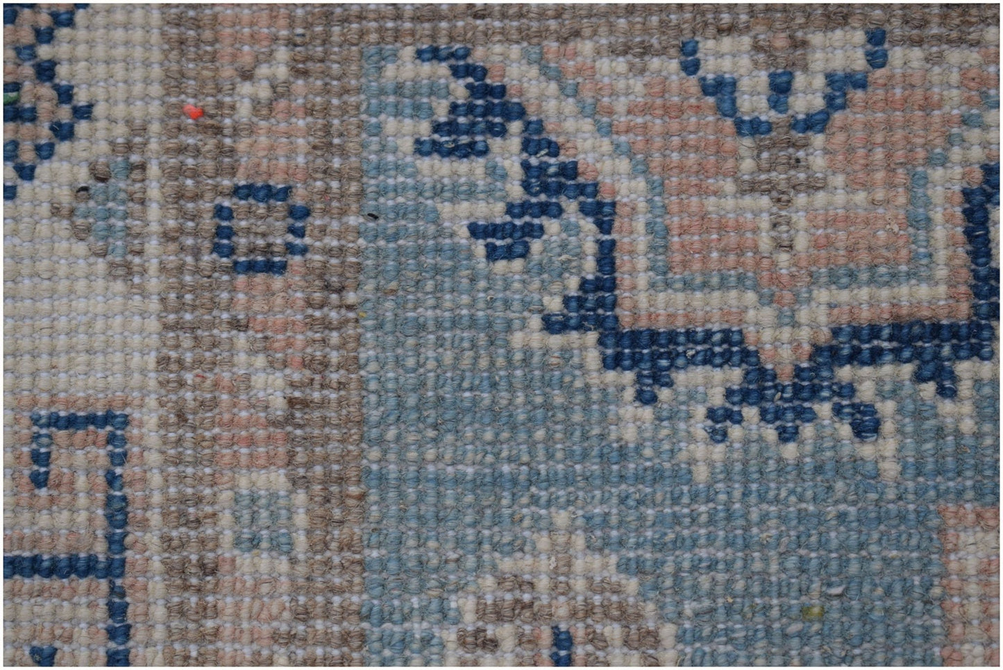 A close-up of a handmade Afghan Kazakh runner featuring geometric blue patterns on a beige field.
