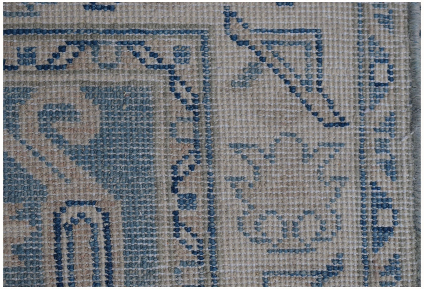 A close-up view of an Afghan Kazakh runner rug featuring blue geometric patterns on a beige base.