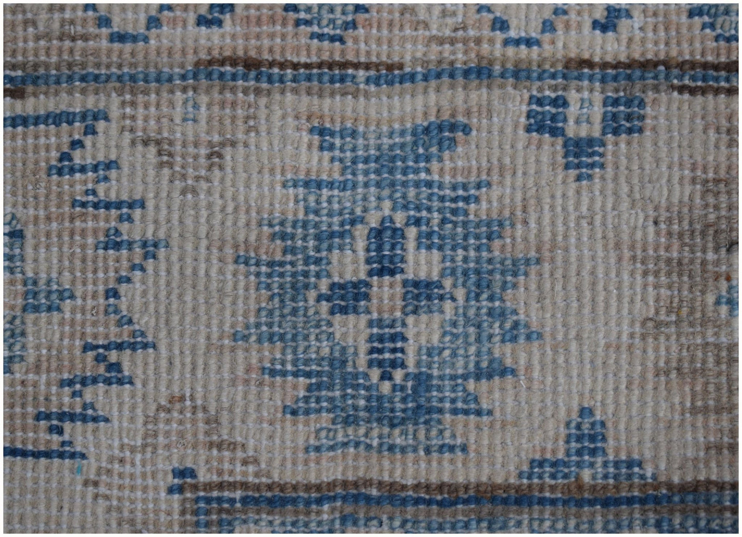A close-up of a handmade Afghan Kazakh runner featuring blue geometric motifs on a beige wool field.
