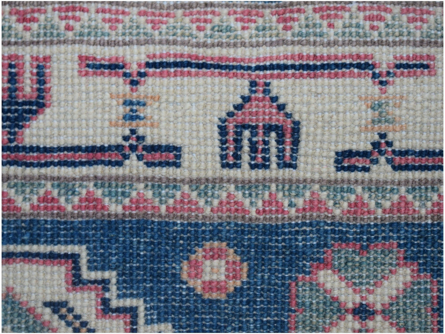 A close-up of an Afghan Kazakh runner featuring traditional geometric motifs in blue, pink, and tan.