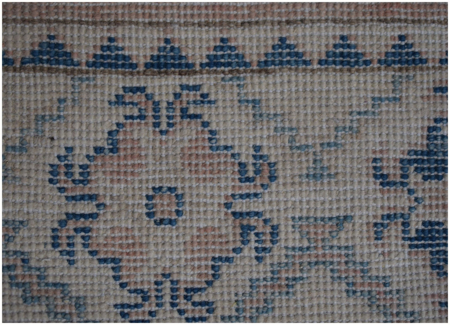 A close-up of a handmade Afghan Kazakh runner featuring a geometric floral pattern in blue and beige.