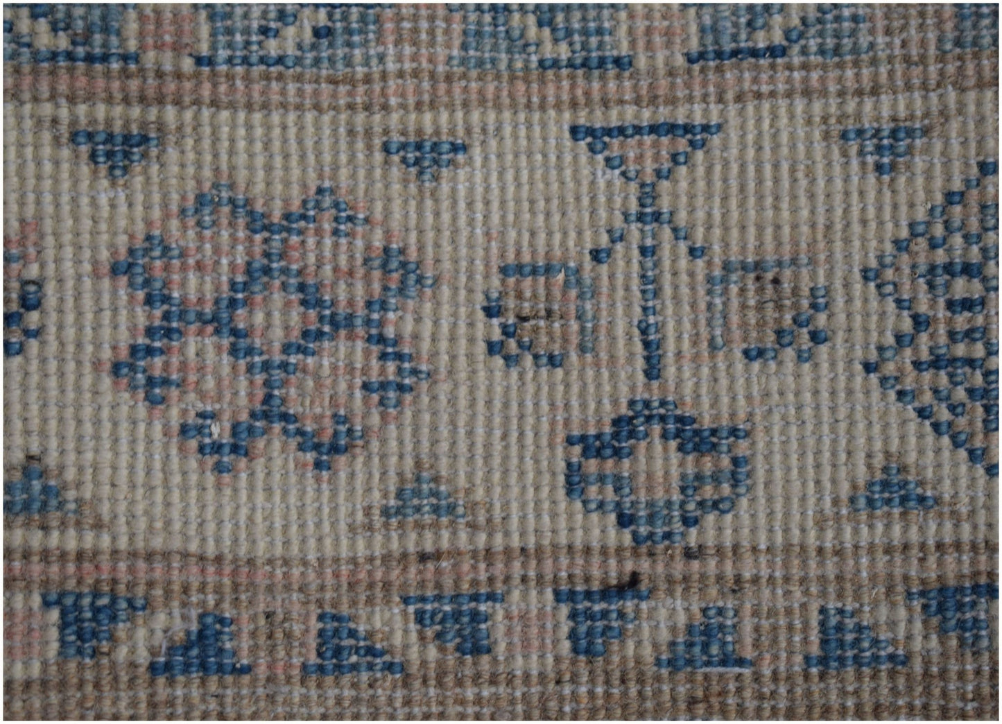 A close-up of a handmade Afghan Kazakh runner featuring a beige wool pile with blue geometric motifs.