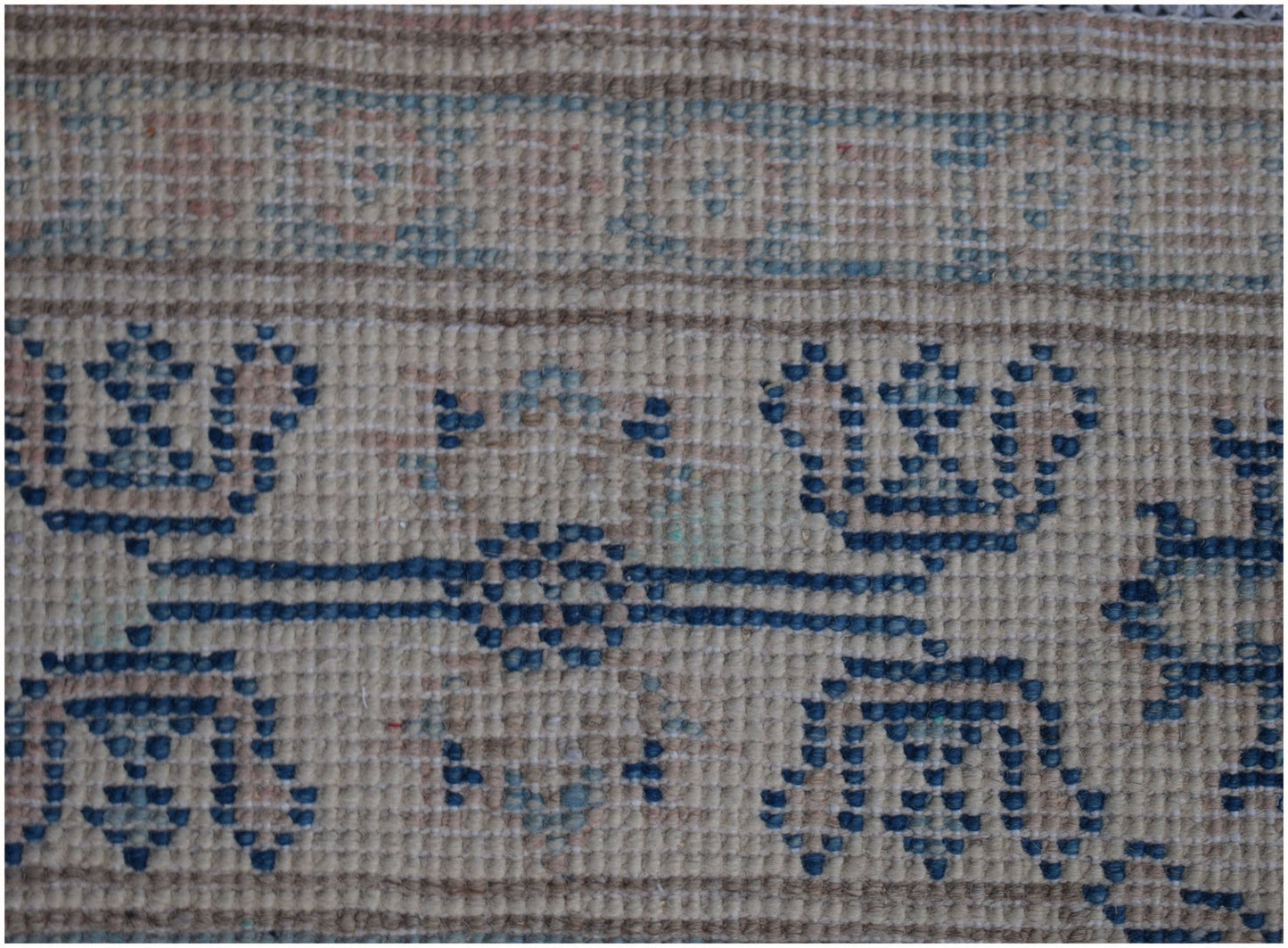 A close-up of an Afghan Kazakh runner rug featuring a beige background with blue geometric motifs.