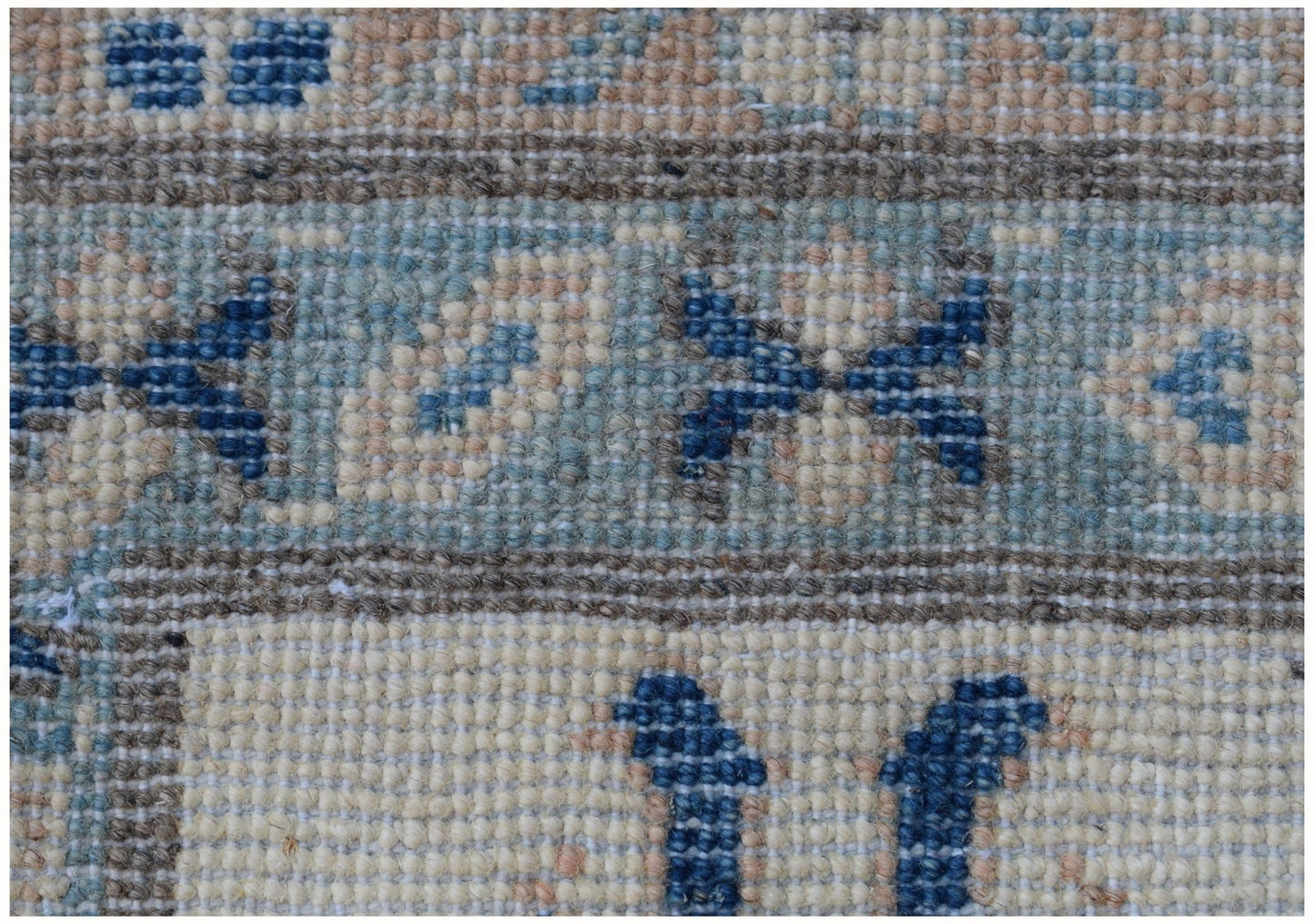 A close-up view of a handmade Afghan Kazakh rug featuring geometric blue patterns on a beige base.