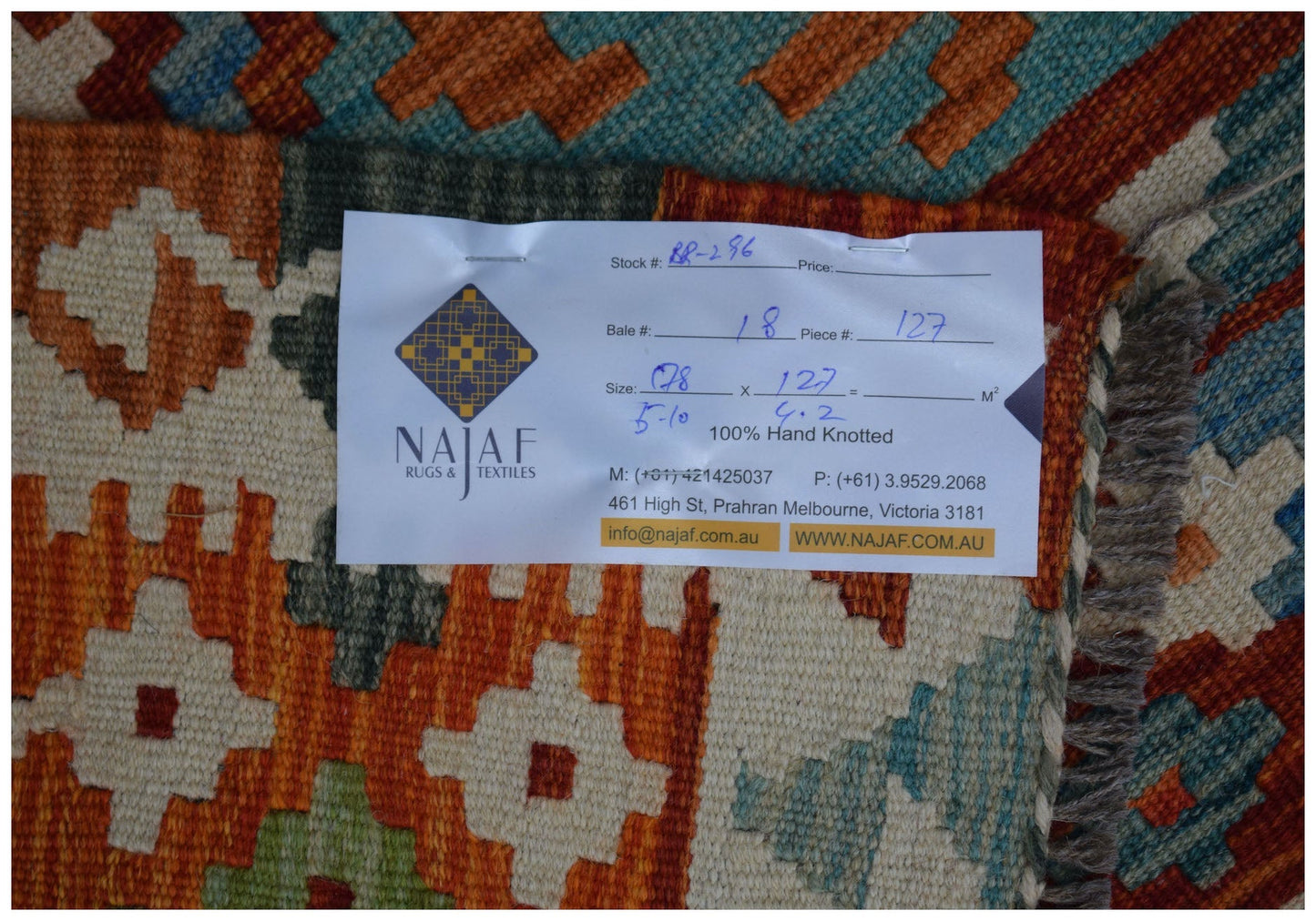 An Afghan Maimana kilim rug featuring a geometric pattern in orange, teal, and cream wool.