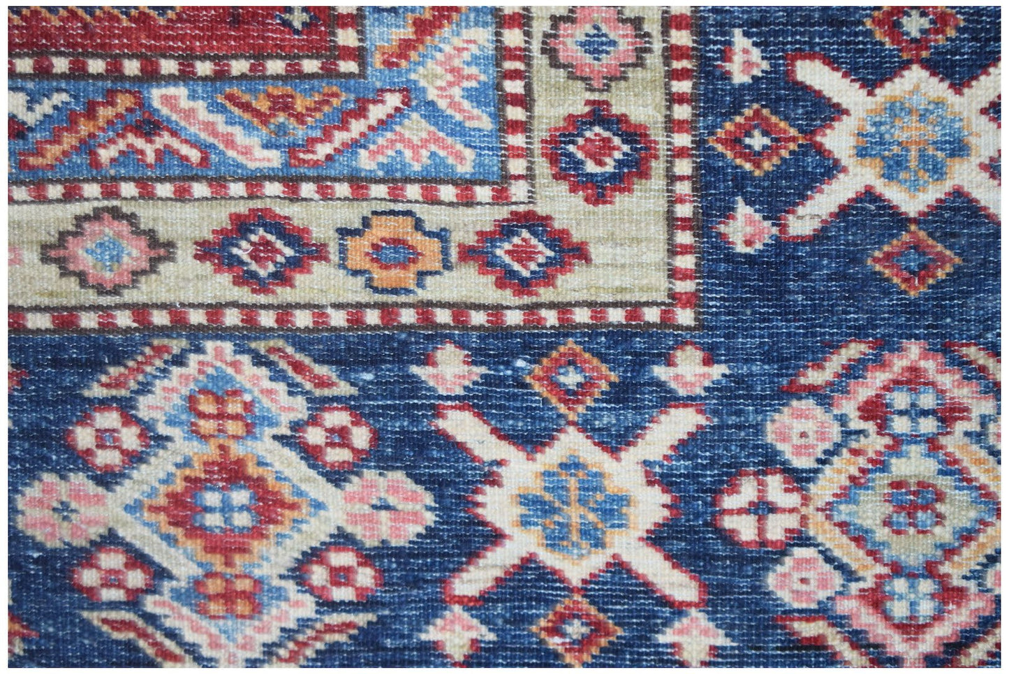 A close-up of an Afghan Super Kazakh rug featuring traditional geometric patterns in blue and red.