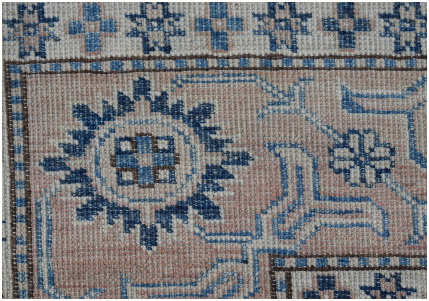 A close-up of an Afghan Super Kazakh rug featuring geometric blue and cream patterns on a pink base.