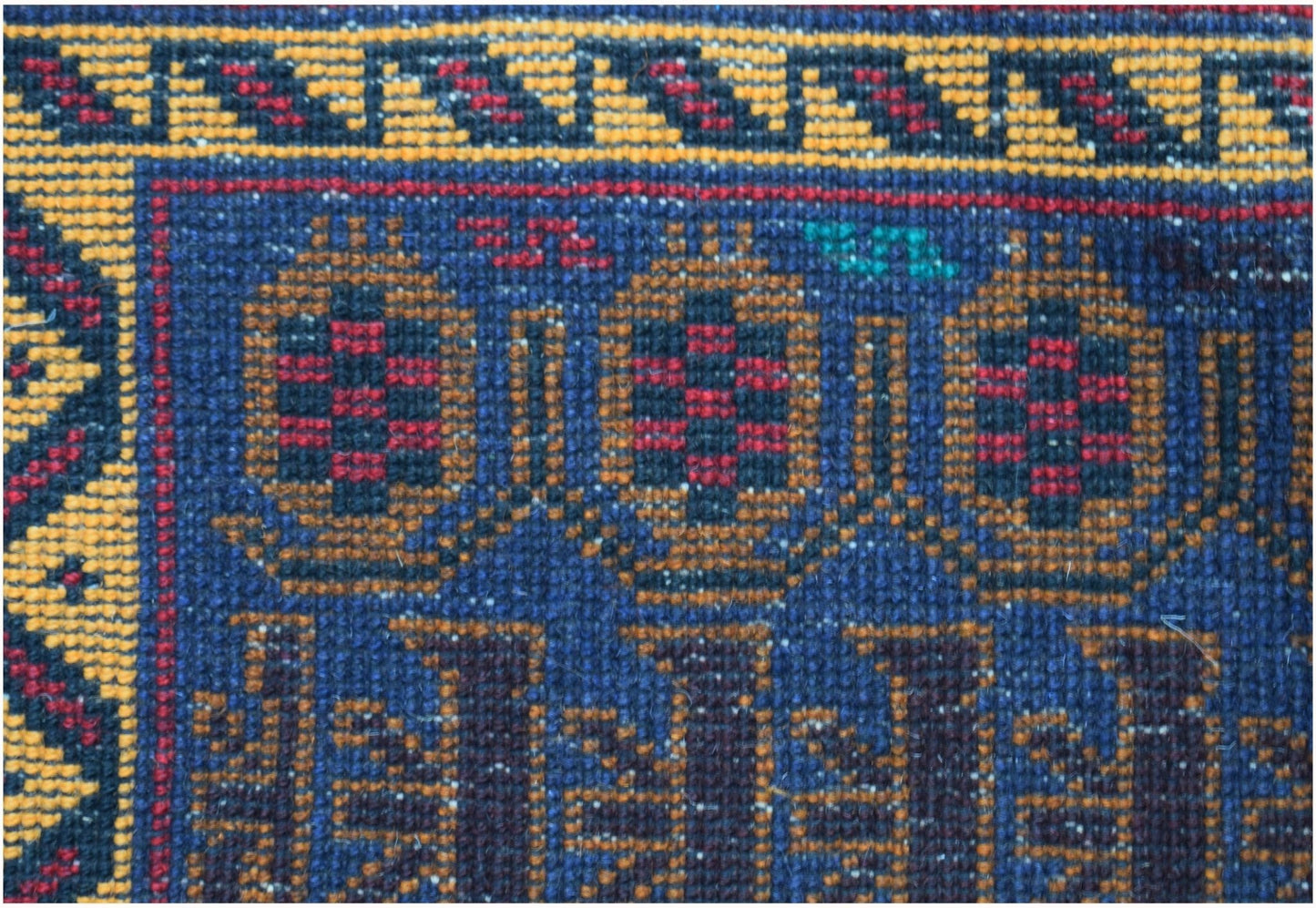 A close-up of a handmade Afghan wool rug featuring geometric patterns in blue, red, and gold.