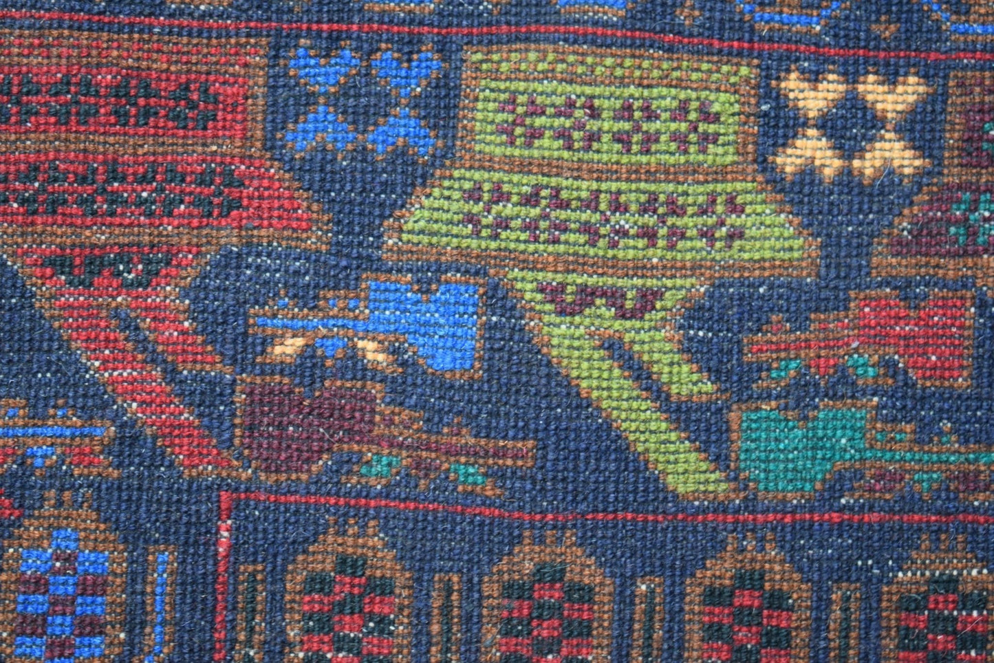 A close-up of a handmade Afghan wool rug featuring intricate geometric and symbolic patterns.