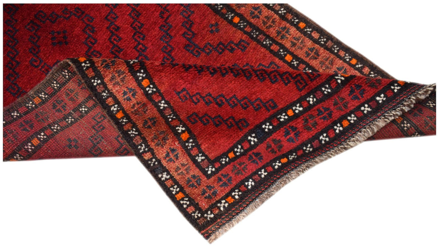 A vintage handmade Afghan Baluch rug featuring a red field with dark geometric patterns and fringe.