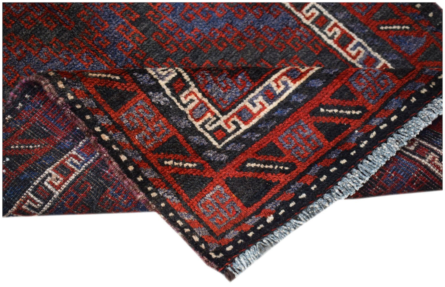 A folded vintage Afghan Baluch rug featuring geometric patterns in dark red, blue, and ivory wool.