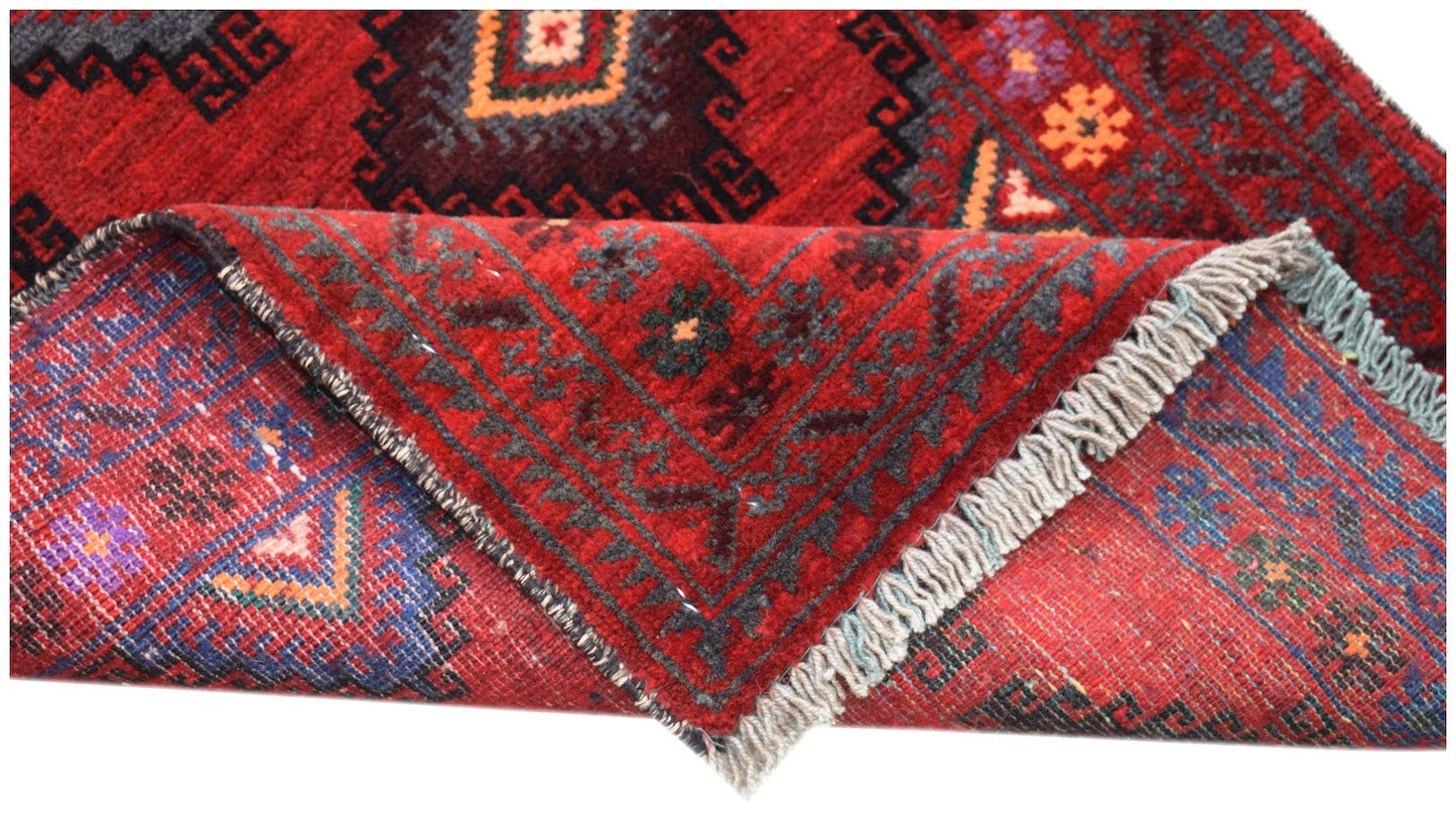 A vintage handmade Afghan Baluch wool rug with a red geometric pattern and fringed edges.