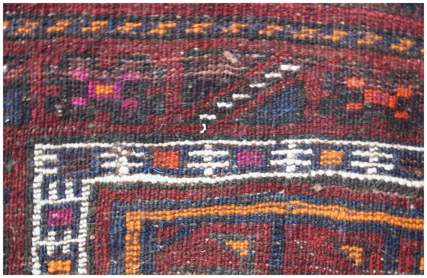 A close-up of a vintage handmade Afghan Baluch wool rug featuring geometric patterns in red and blue.