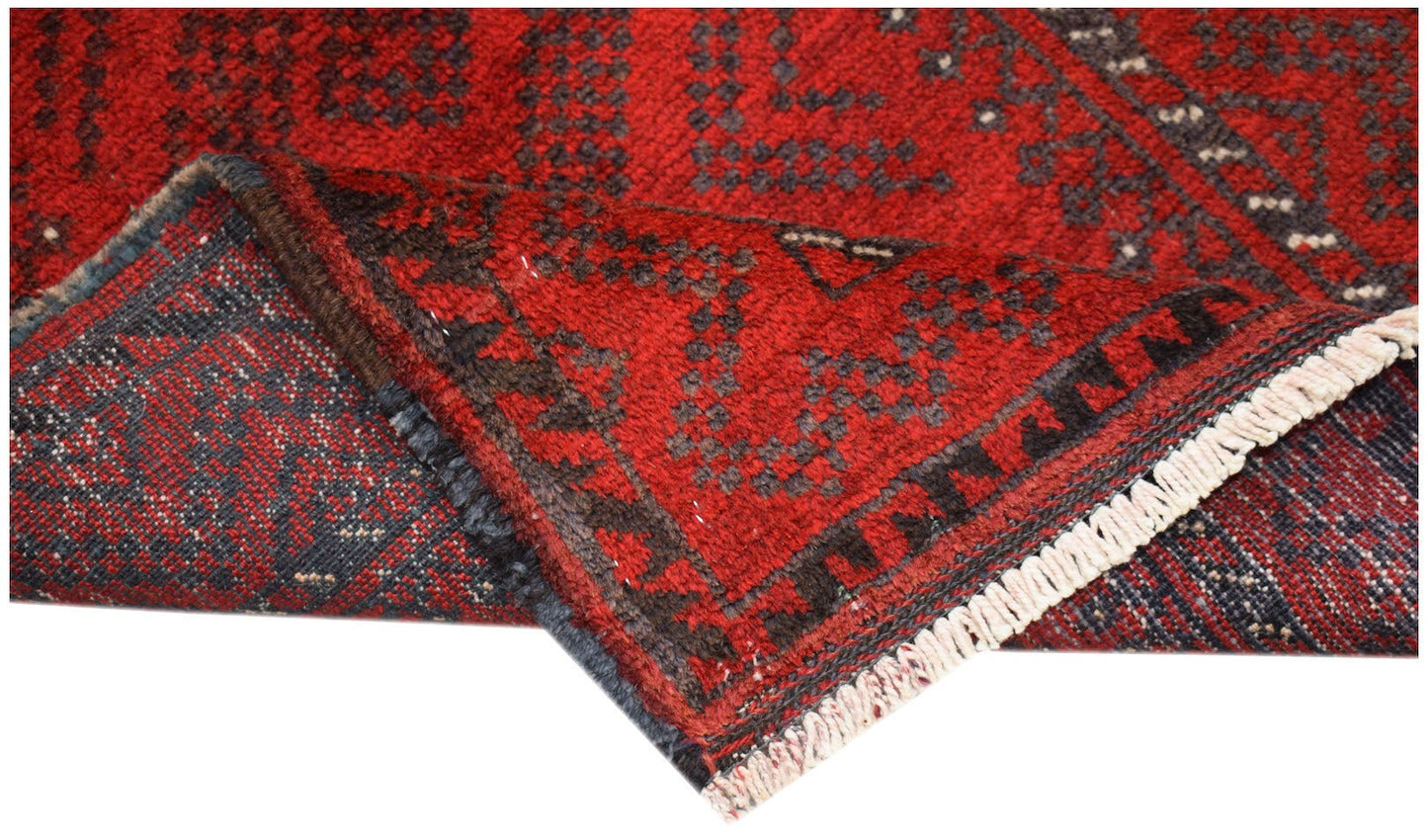 A vintage Afghan Baluch wool rug with a red geometric pattern and a fringed edge.