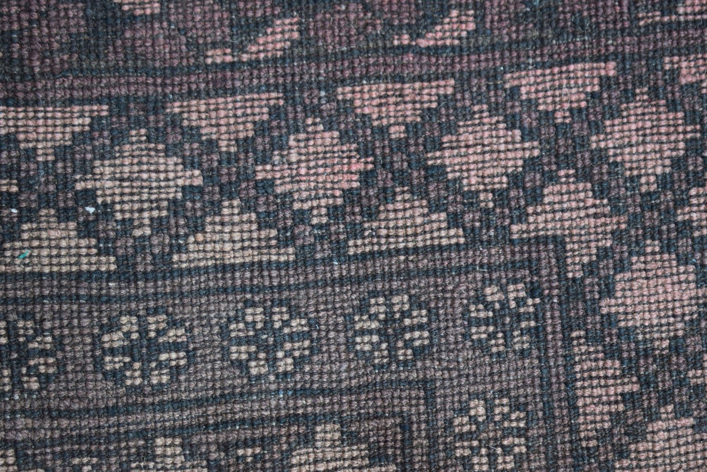 A close-up of a vintage Afghan Turkmen rug featuring geometric patterns in dark brown and tan wool.