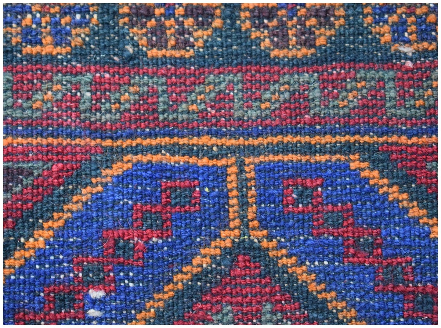 A close-up of a vintage Afghan Baluch wool rug featuring geometric patterns in blue, red, and orange.