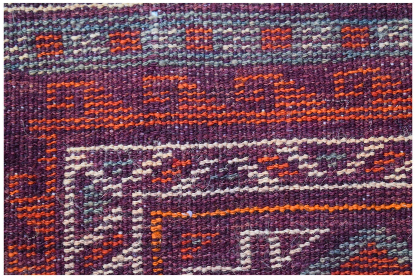 A close-up of a vintage Afghan Baluch rug featuring geometric patterns in deep red and orange wool.