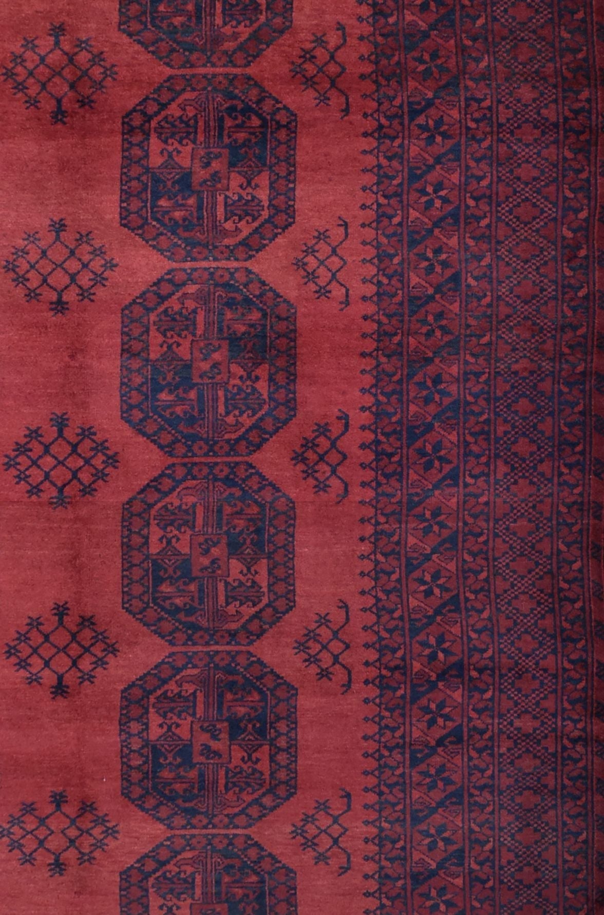 A vintage handmade Afghan Turkmen rug featuring dark blue geometric octagons on a red wool field.