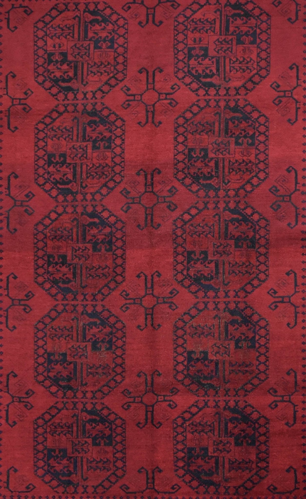 A vintage Afghan Turkmen rug featuring a repeating geometric pattern in deep red and black wool.