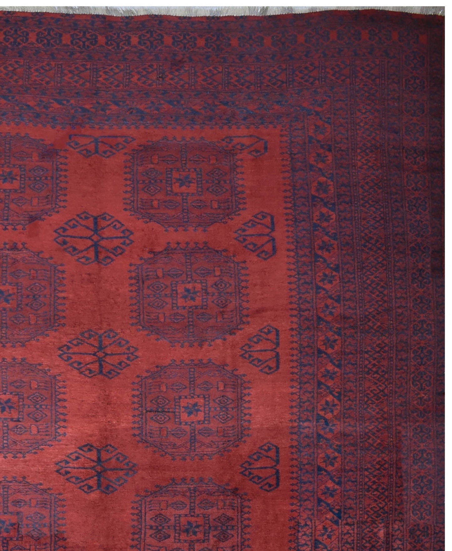 A vintage handmade Afghan Turkmen rug featuring geometric blue motifs on a deep red wool field.
