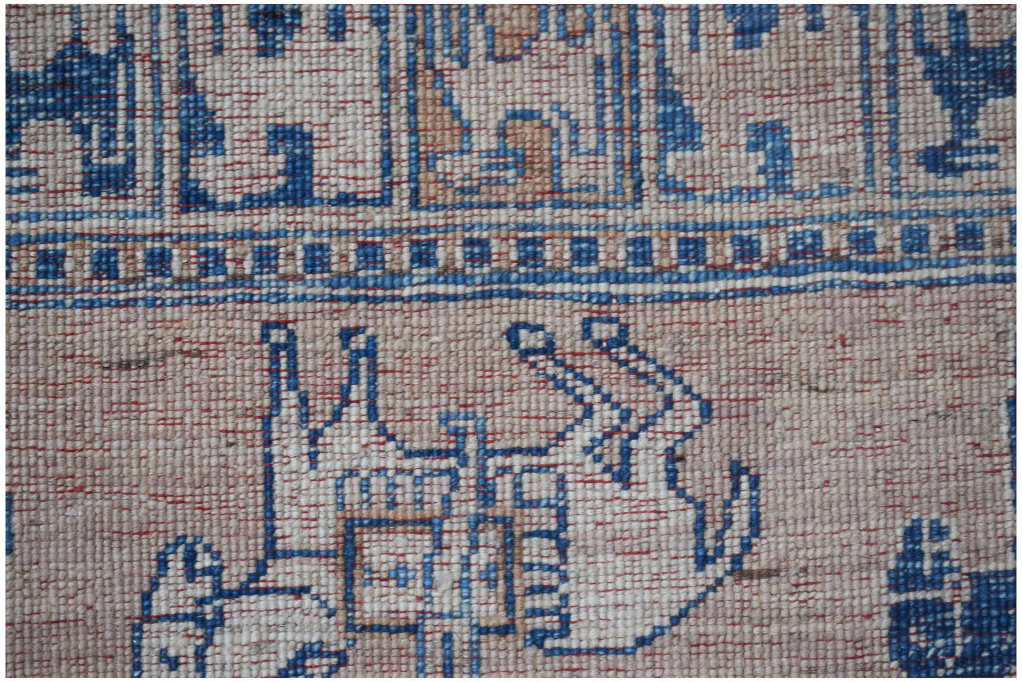 A close-up of a handmade Afghan Chobi rug featuring blue geometric animal motifs on a beige field.