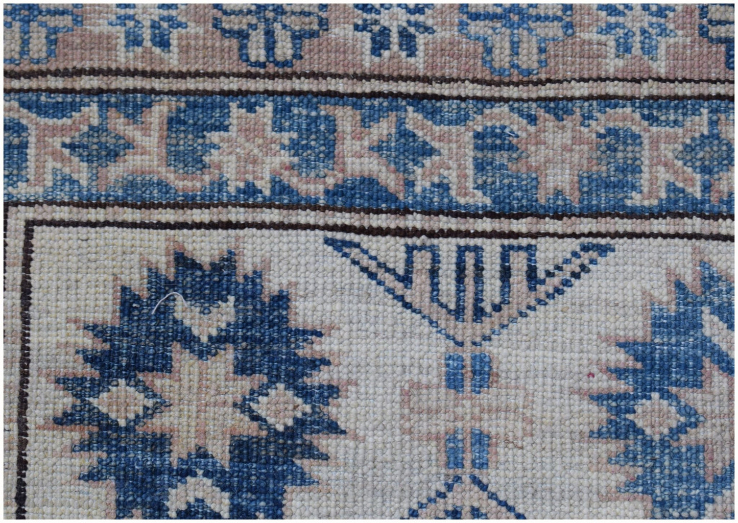 A close-up of an Afghan Super Kazakh rug featuring traditional blue and beige geometric motifs.