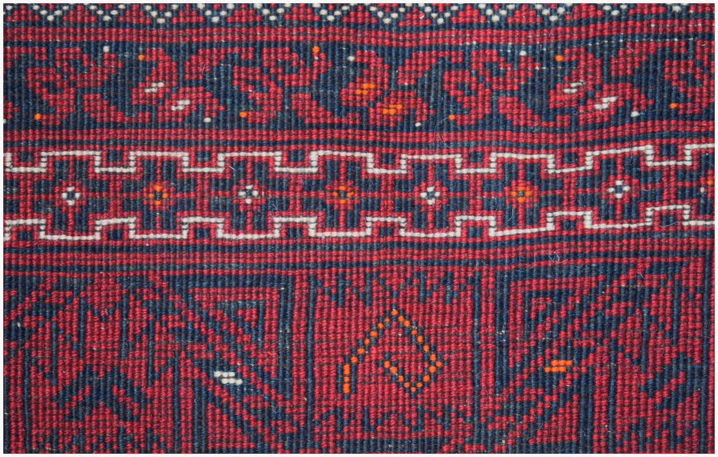 A close-up of a vintage Afghan Turkmen rug featuring geometric patterns in red and dark blue wool.