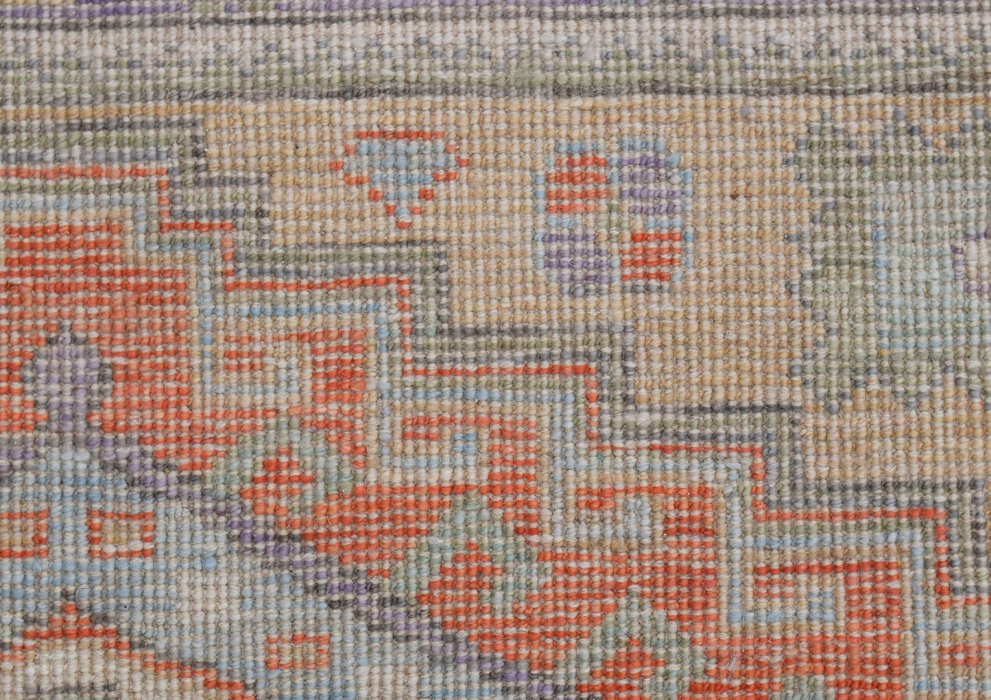 A close-up of a handwoven transitional Oushak rug featuring geometric patterns in orange and blue.