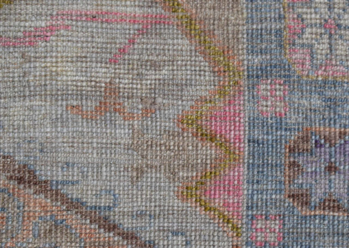 A close-up view of a handwoven wool rug featuring a transitional floral pattern in soft colors.