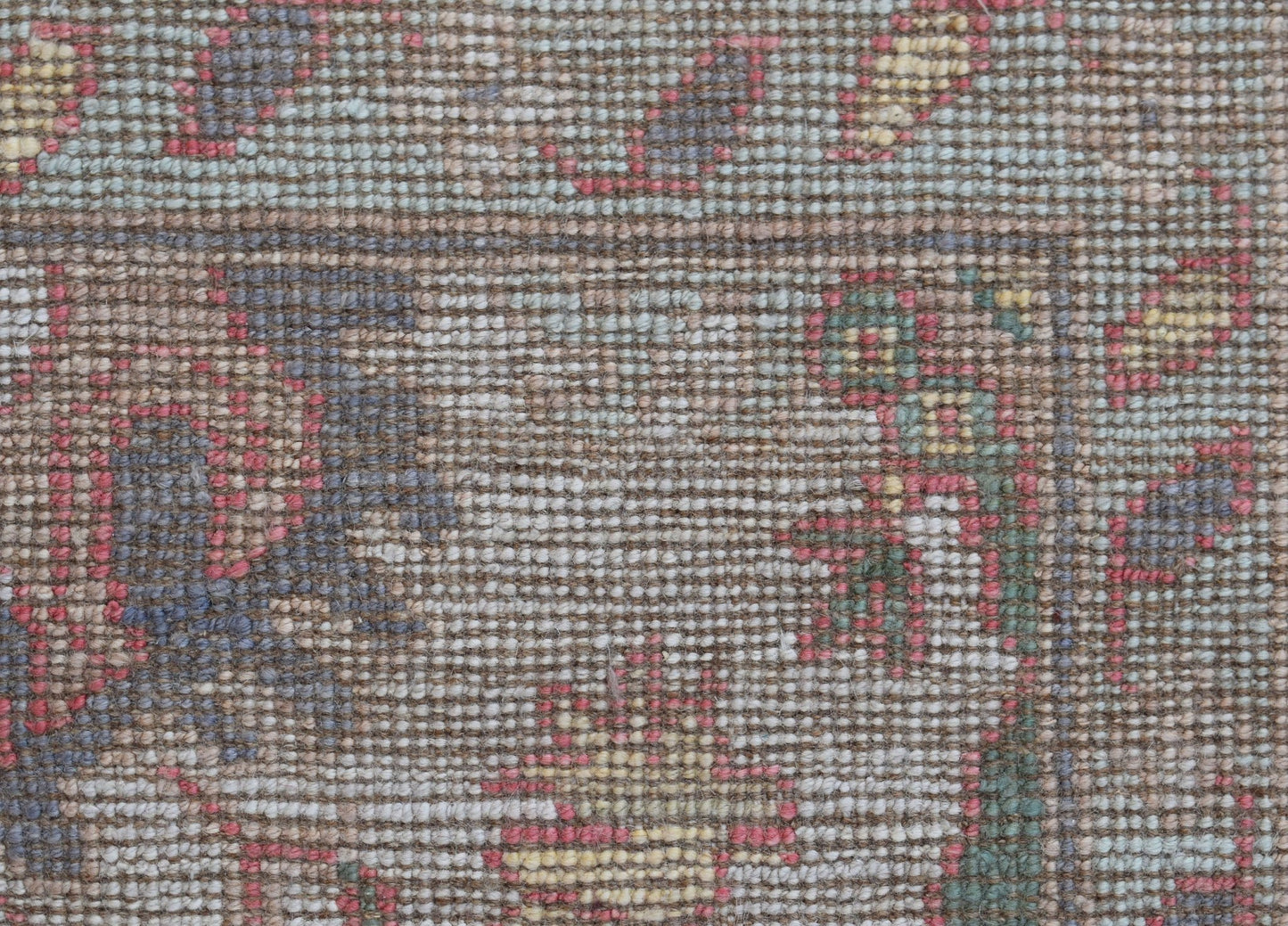 A close-up of a handwoven Oushak rug featuring a floral pattern in muted tones on a brown base.