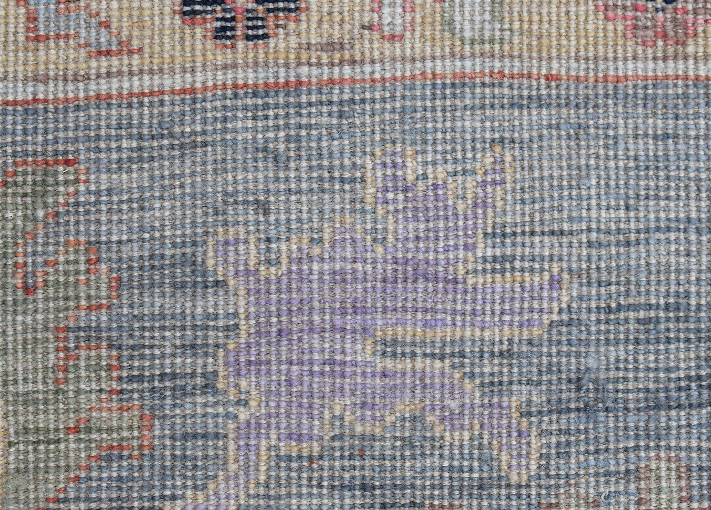A close-up of a handwoven wool rug featuring a floral pattern in blue, purple, and beige tones.