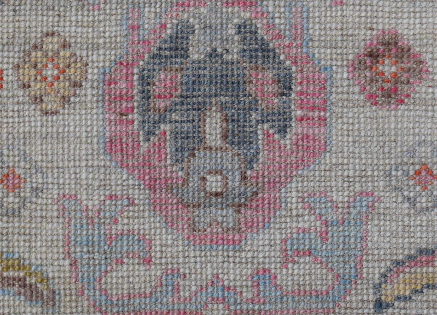 A close-up of a handwoven wool rug featuring a floral pattern in pink, blue, and neutral tones.