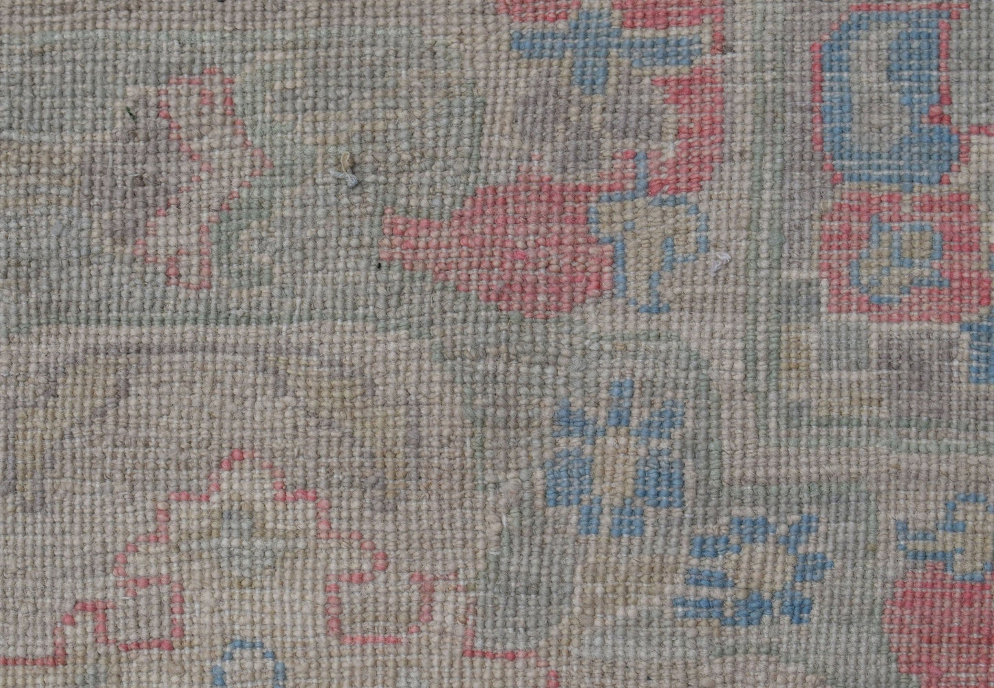 A close-up of a handwoven Oushak rug featuring a floral pattern in soft blue and pink tones.
