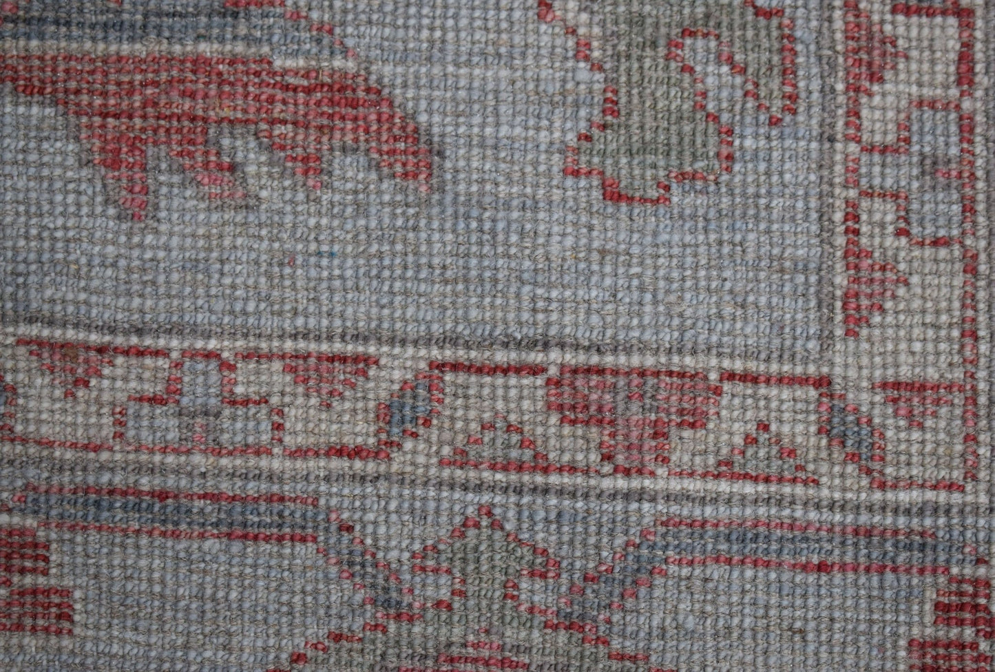 A close-up of a handwoven Oushak rug featuring a traditional floral pattern in red and grey tones.