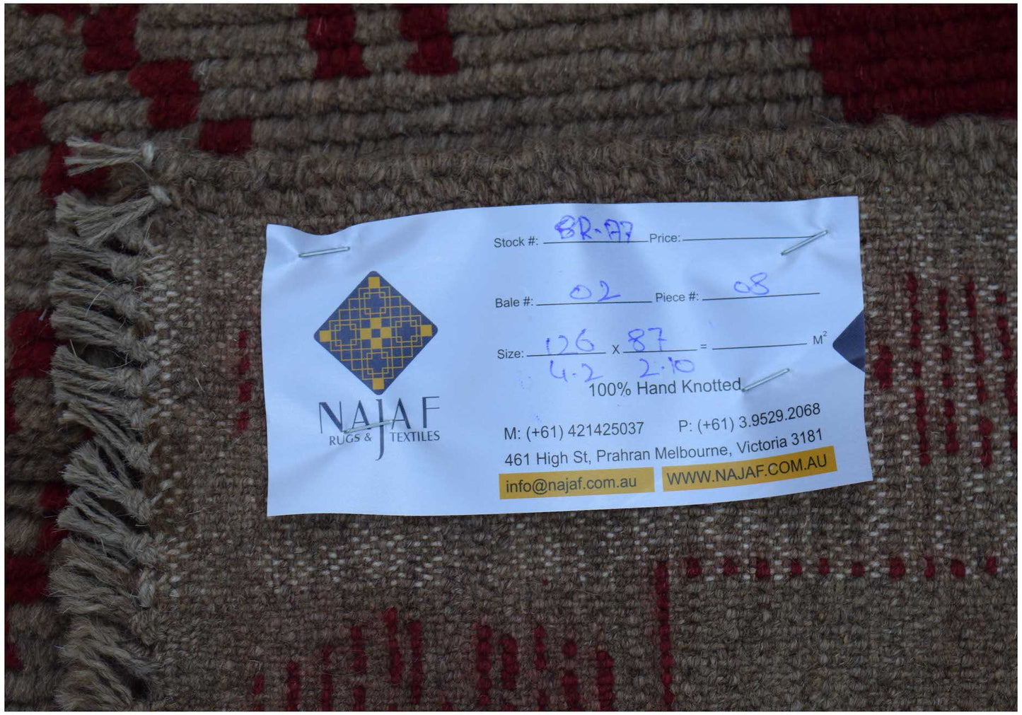 A handmade Afghan Pashm rug featuring a geometric pattern in dark red and brown wool.