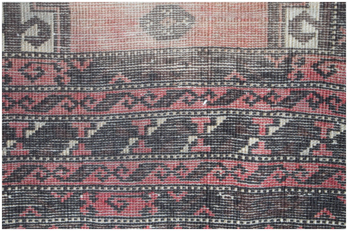 A close-up of a vintage Afghan Baluch rug featuring intricate geometric patterns in red and black.