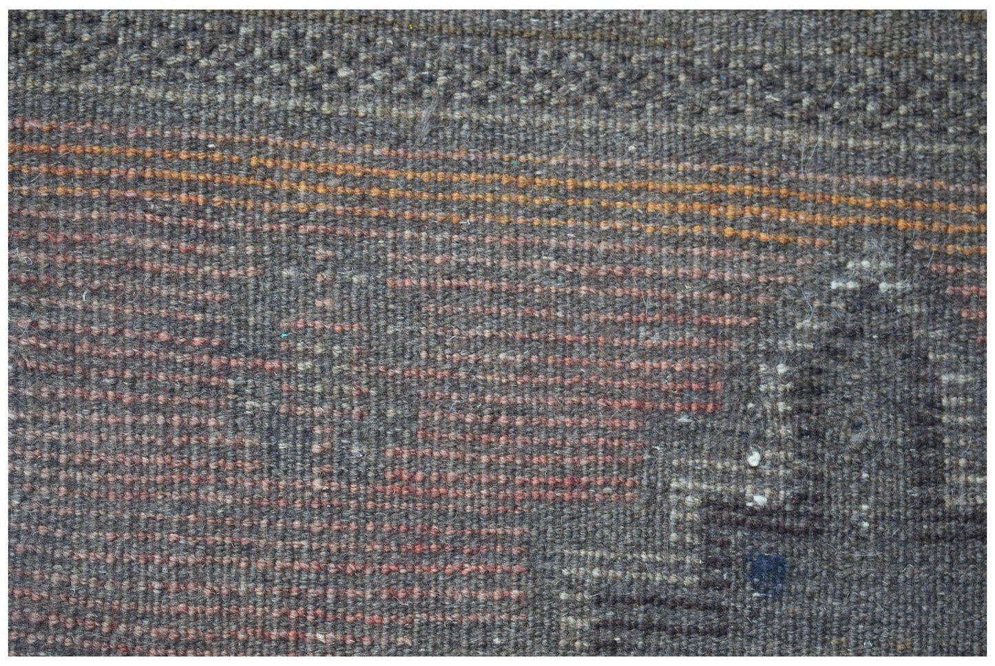 A close-up of a handmade Afghan Baluch rug featuring a dark wool texture with subtle orange accents.