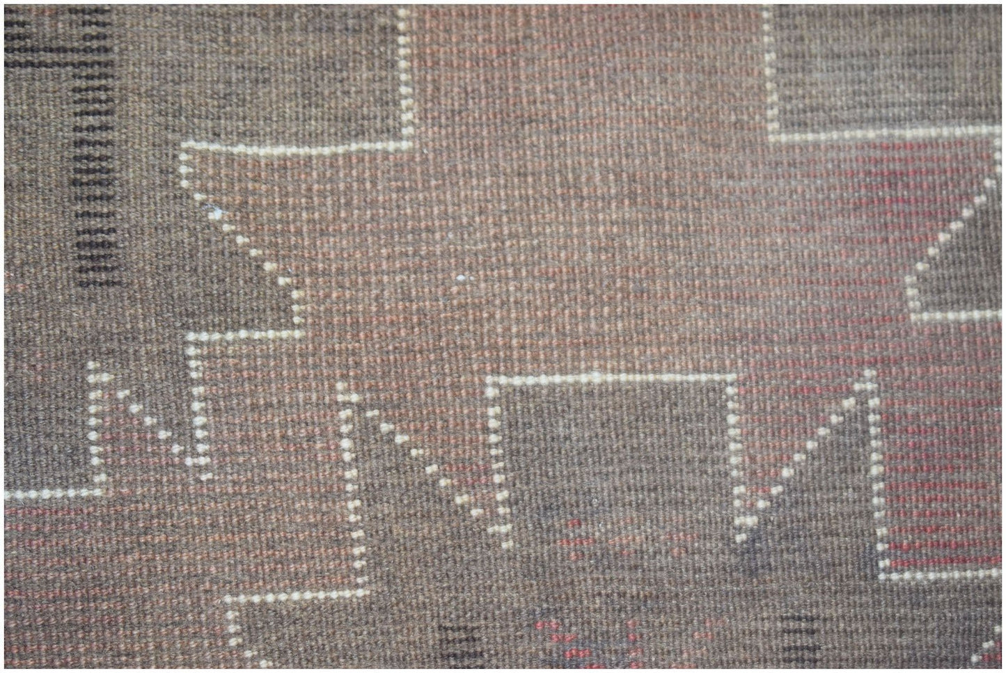 A close-up of a handmade Afghan Baluch rug featuring geometric patterns in brown and red wool.