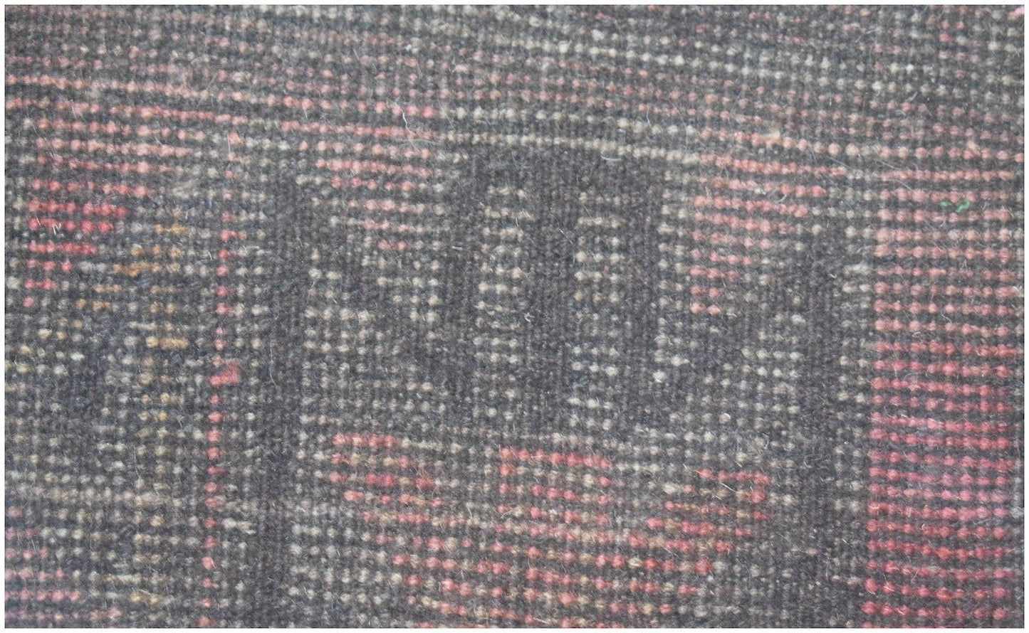 A close-up of a handmade Afghan Baluch rug featuring a dark geometric pattern with red accents.