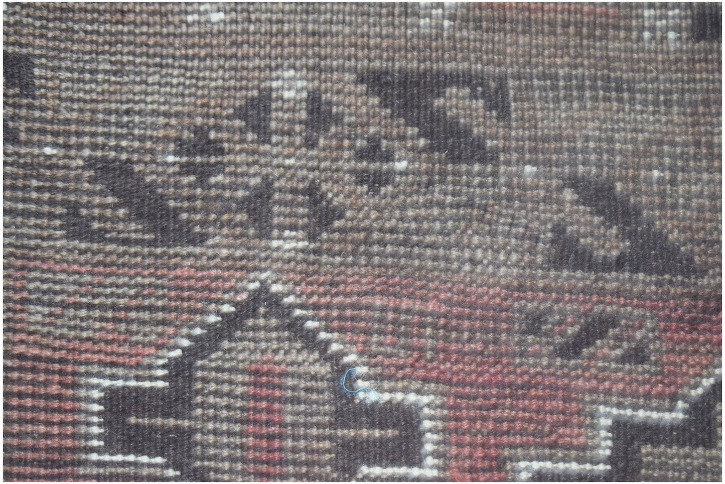 A close-up of a handmade Afghan Baluch rug featuring geometric patterns in brown, red, and white.