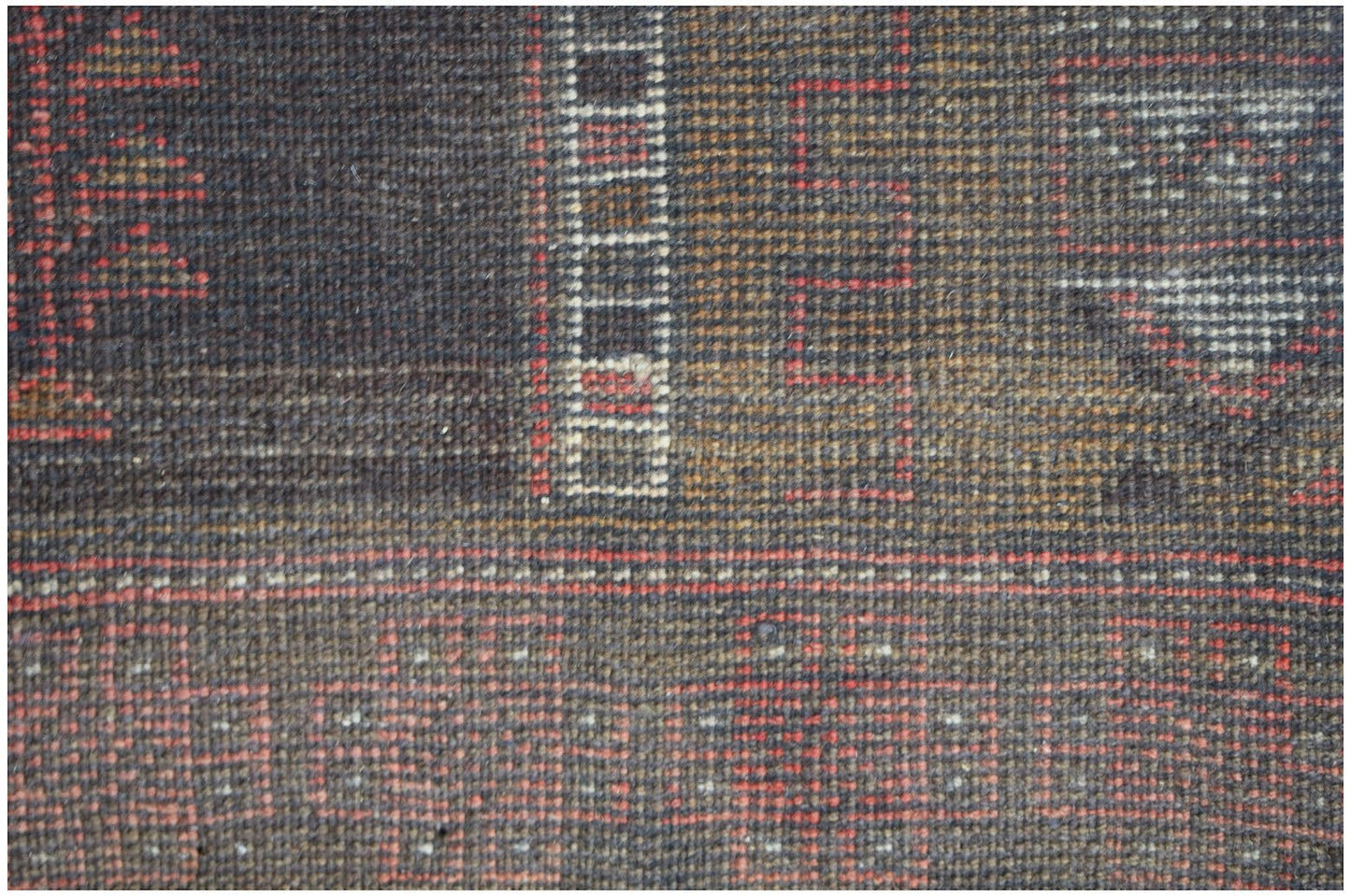 A close-up of a handmade Afghan Baluch rug featuring geometric patterns in red, brown, and cream.