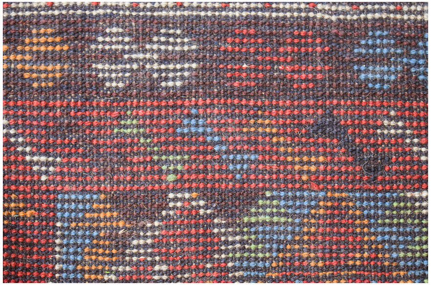 Handmade Afghan Pashm rug featuring a dark wool base with geometric patterns in red, blue, and gold.