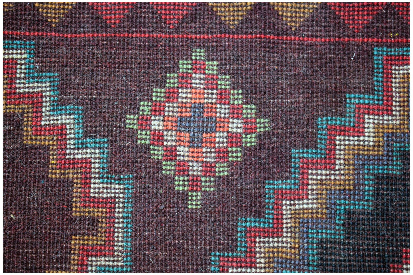 A handmade Afghan Pashm rug featuring a dark brown field with geometric diamond and zigzag patterns.
