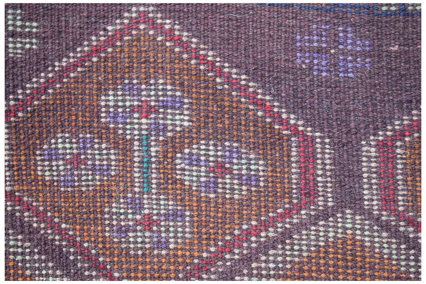 A close-up of a handmade Afghan Pashm rug featuring intricate geometric patterns in dark wool.