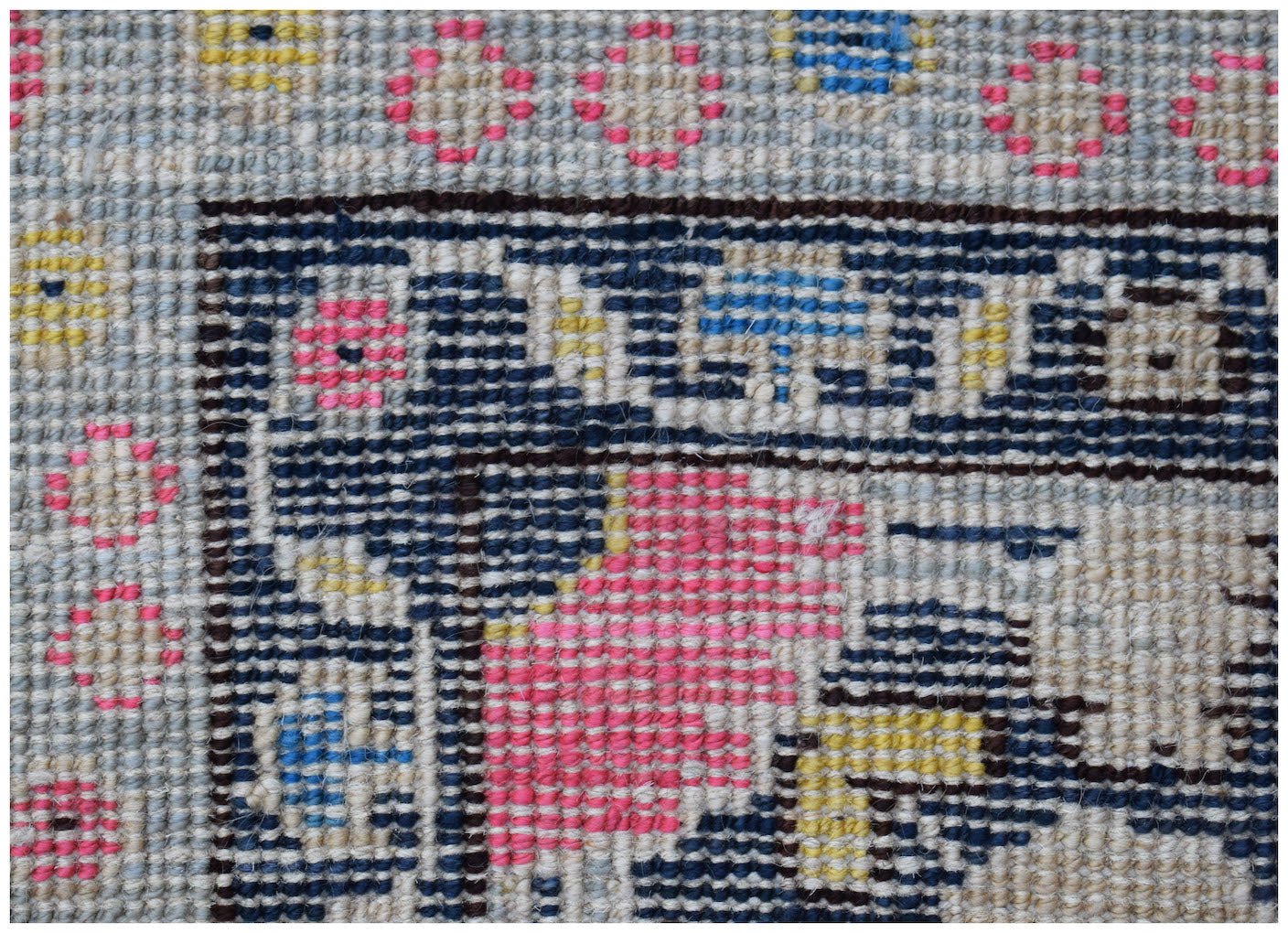 A close-up of a handmade Afghan wool rug featuring a geometric pattern in pink, blue, and yellow.