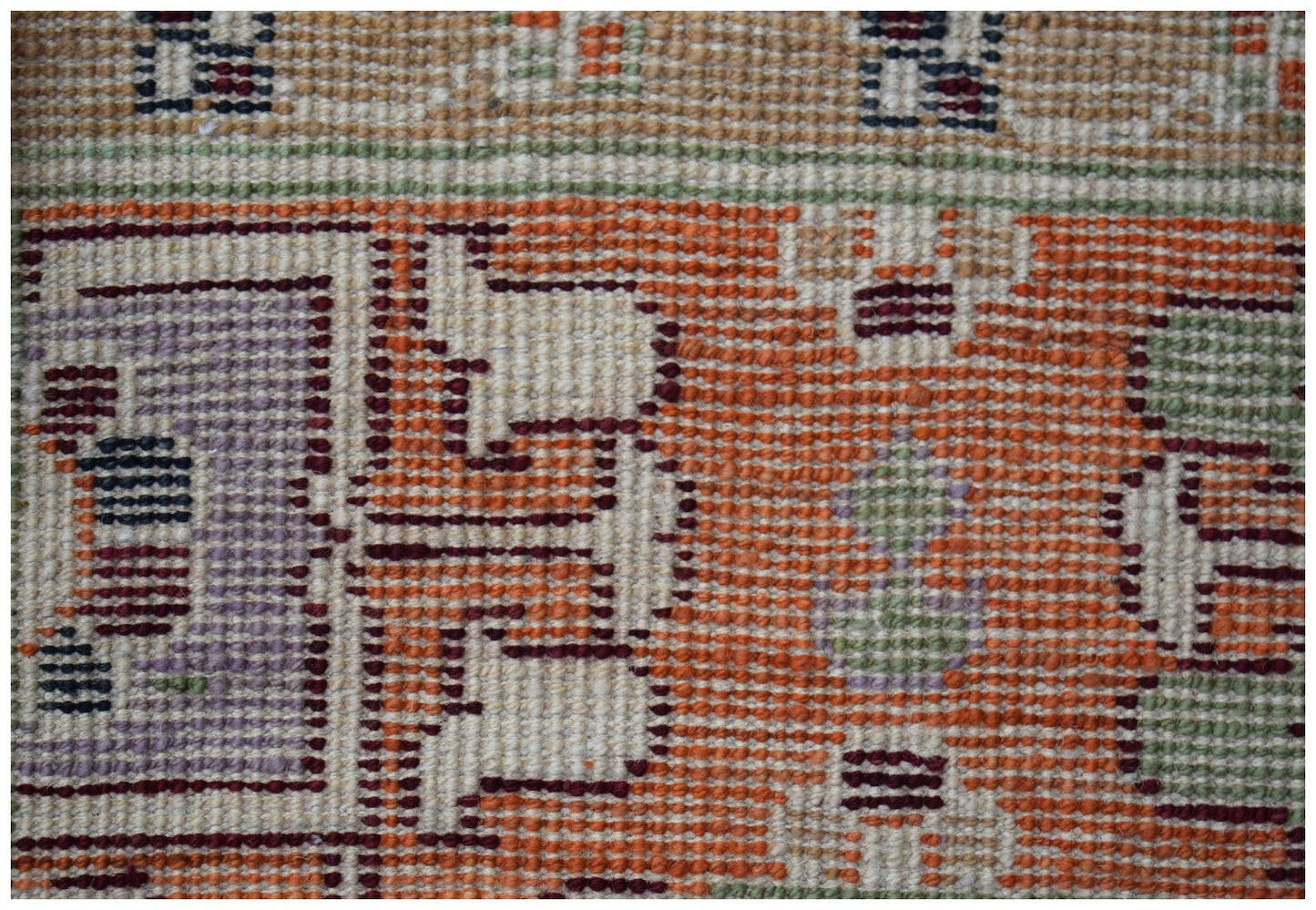 A close-up of a handmade Afghan wool rug featuring geometric tribal patterns in orange and purple.
