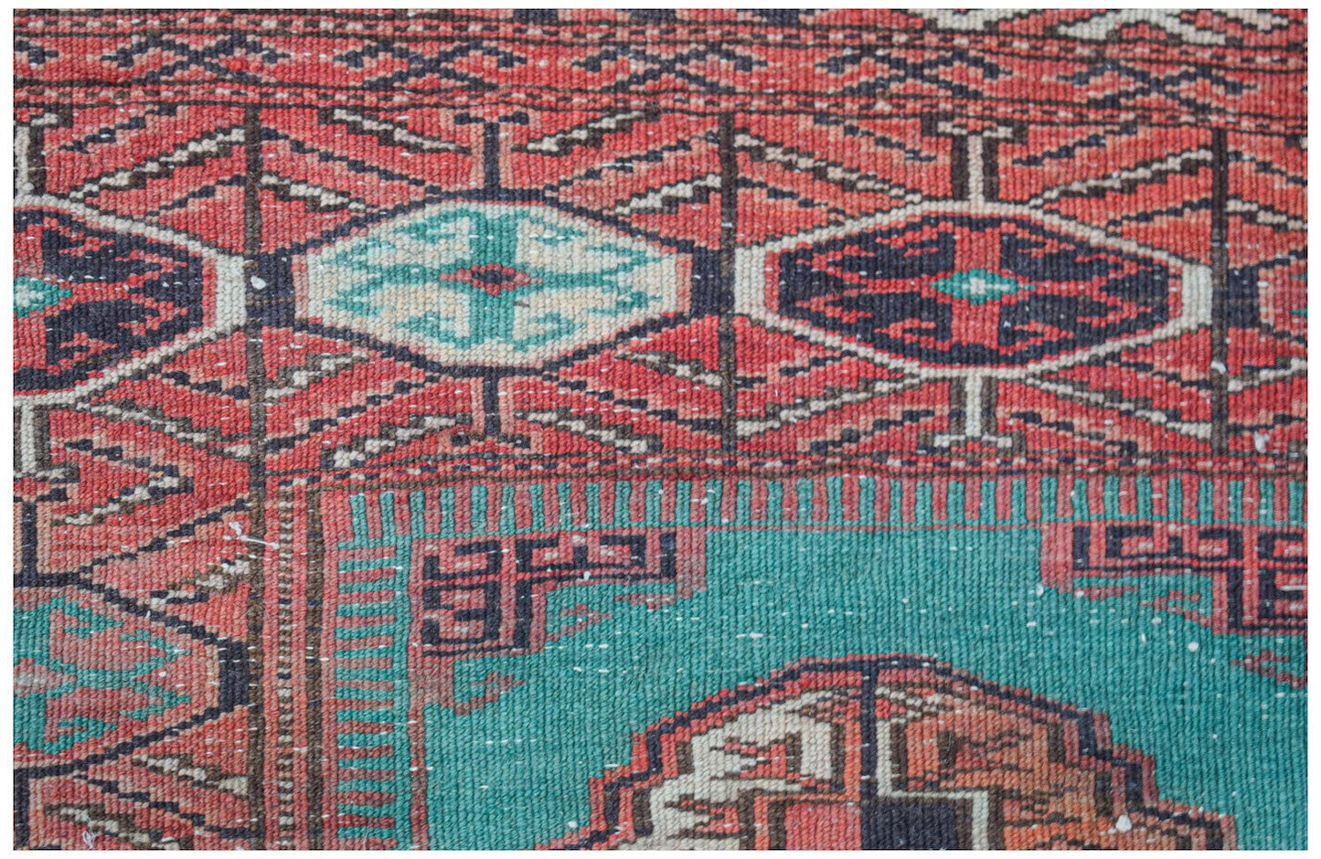 A vintage handwoven Afghan Turkmen rug featuring geometric patterns in red, teal, and black.