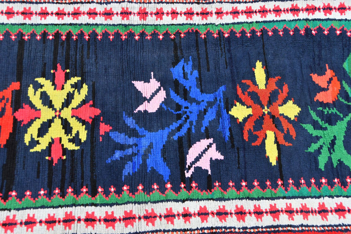A vintage Kurdish Herki runner featuring vibrant tribal floral motifs on a dark blue wool base.