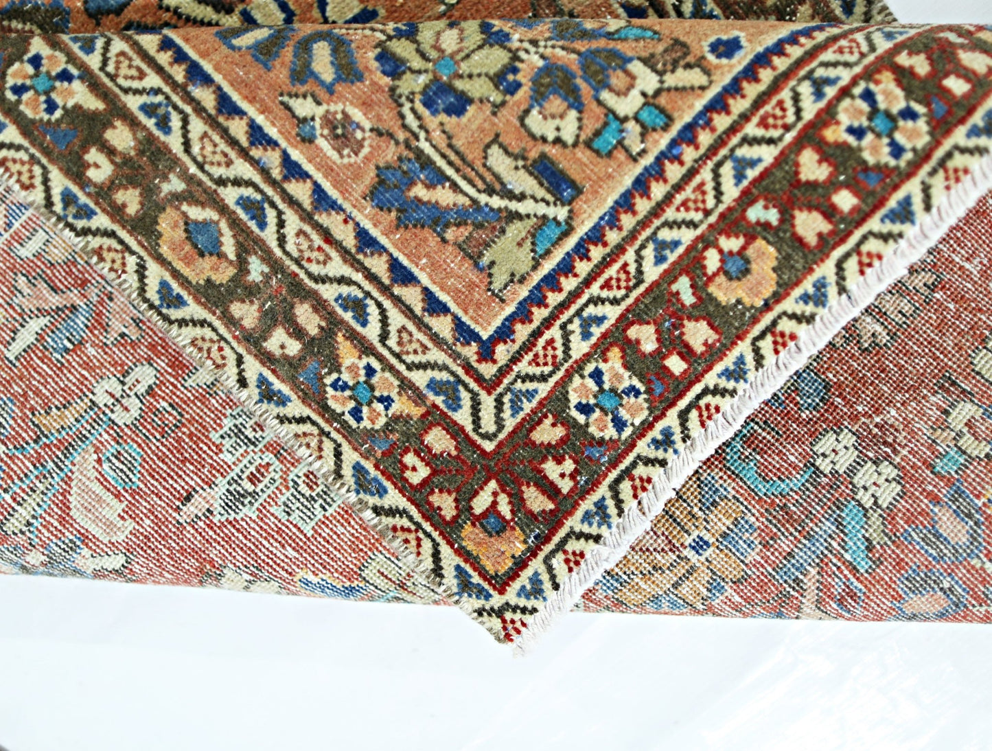 A vintage Persian runner with a folded corner revealing intricate floral patterns in wool.