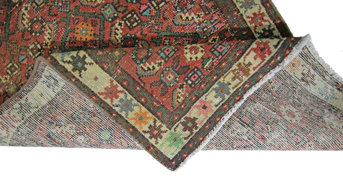 A vintage Persian runner with a red field and geometric patterns, shown folded to reveal the back.